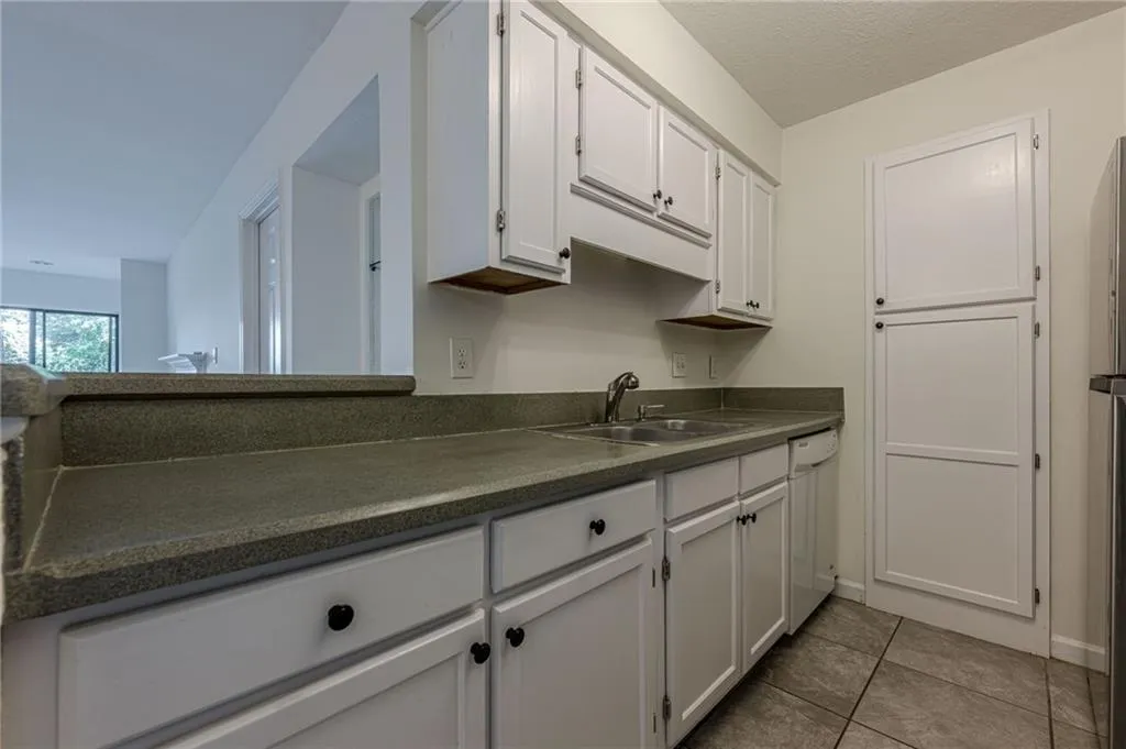 Kitchen with dark countertops, white cabinets, light tile patterned flooring, white dishwasher, and freestanding refrigerator