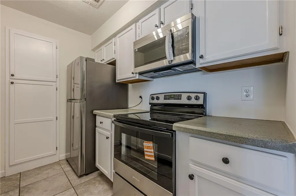 Kitchen featuring appliances with stainless steel finishes, white cabinetry, a textured ceiling, light tile patterned floors, and light countertops