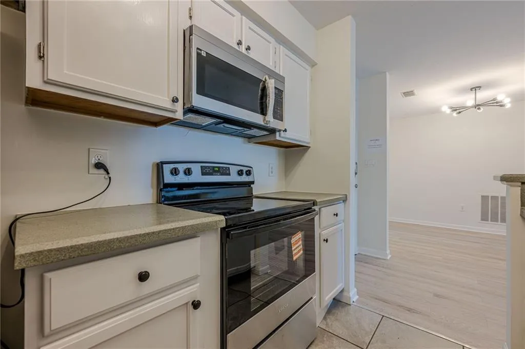 Kitchen with appliances with stainless steel finishes, white cabinets, a chandelier, and light tile patterned floors