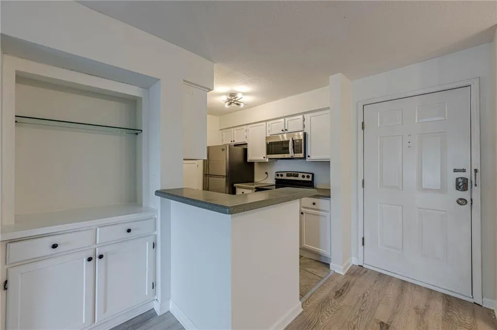 Kitchen featuring white cabinetry, appliances with stainless steel finishes, light wood-style floors, dark countertops, and a peninsula
