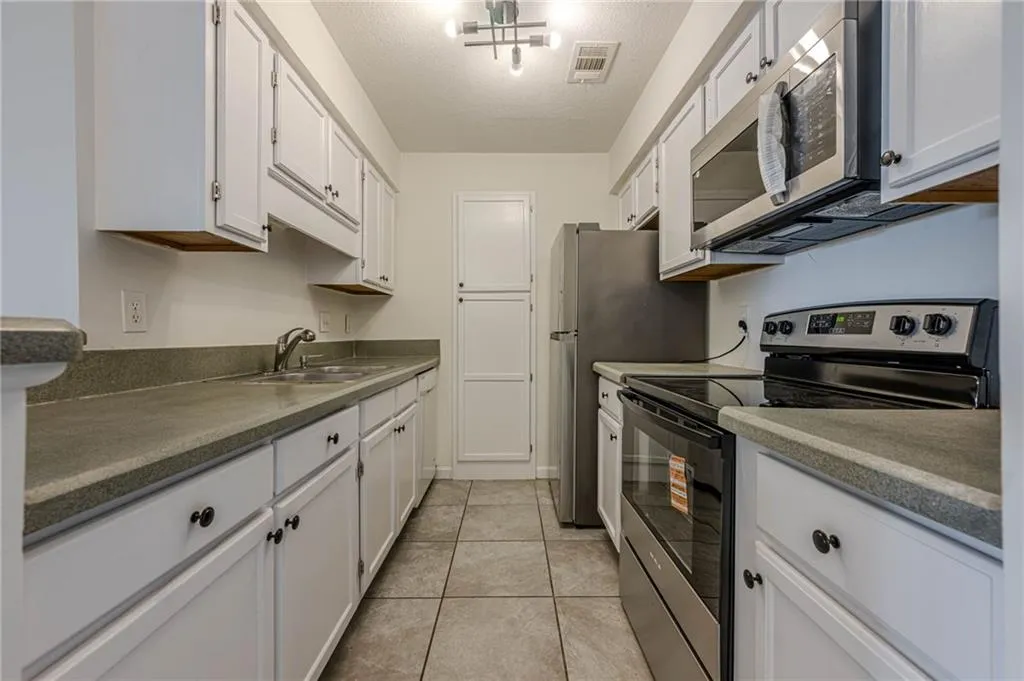 Kitchen featuring appliances with stainless steel finishes, a textured ceiling, white cabinetry, light tile patterned floors, and dark countertops
