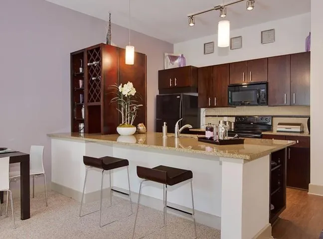 Kitchen with black appliances, a breakfast bar, decorative light fixtures, and light stone countertops