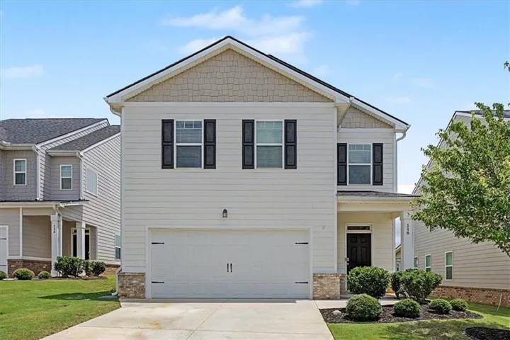 Two-story residence featuring light-colored siding, a prominent two-car garage, and dark window shutters