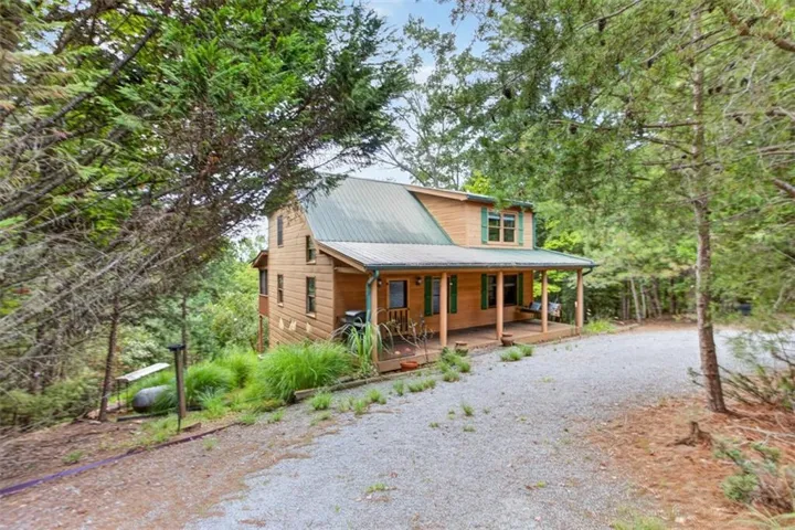 Wood-sided residence with a green metal roof, a covered front porch, and a gravel driveway