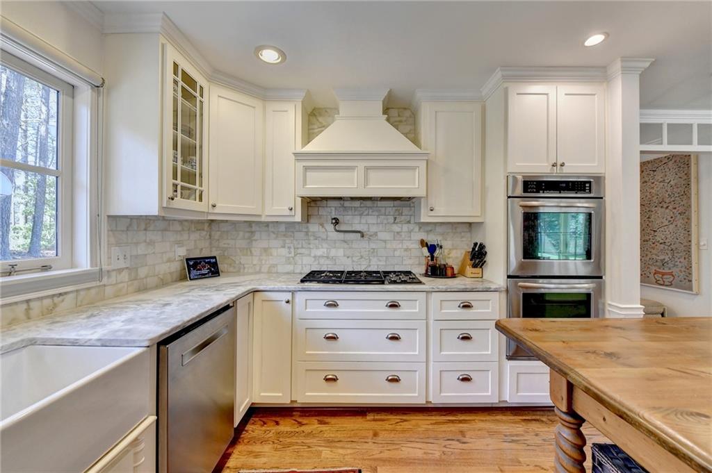 Kitchen with white cabinetry, light hardwood / wood-style flooring, stainless steel appliances, and custom range hood