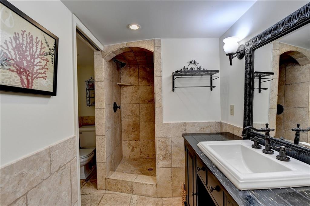 Bathroom featuring oversized vanity, toilet, tiled shower, tile walls, and tile floors