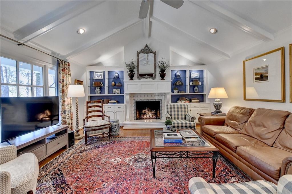Living room featuring a fireplace, lofted ceiling with beams, ceiling fan, and wood-type flooring