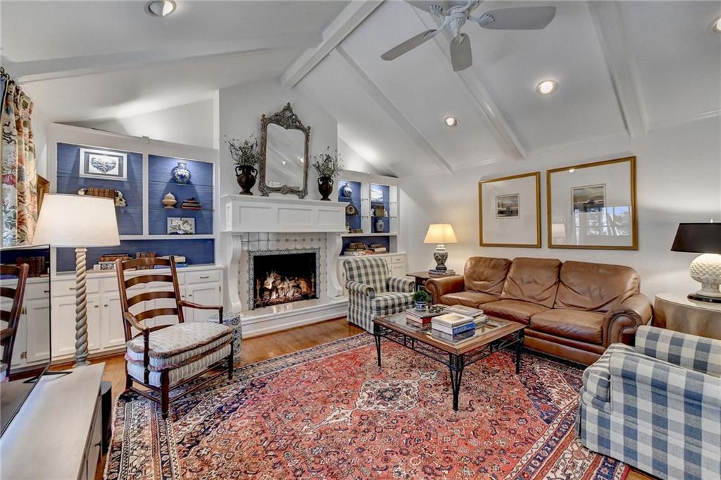 Living room featuring a tiled fireplace, wood-type flooring, ceiling fan, and lofted ceiling with beams