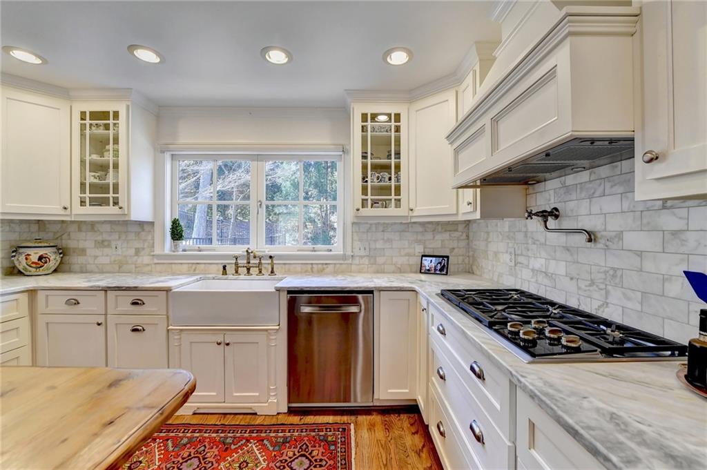 Kitchen with light wood-type flooring, light stone countertops, custom exhaust hood, and backsplash