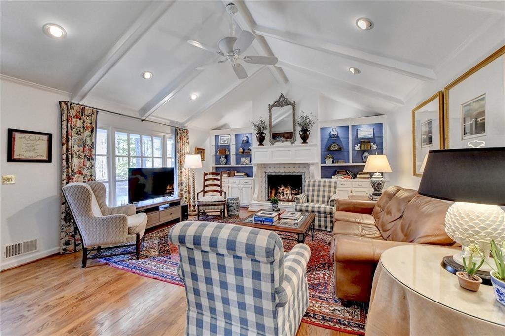 Living room featuring light wood-type flooring, a fireplace, lofted ceiling with beams, ceiling fan, and built in features