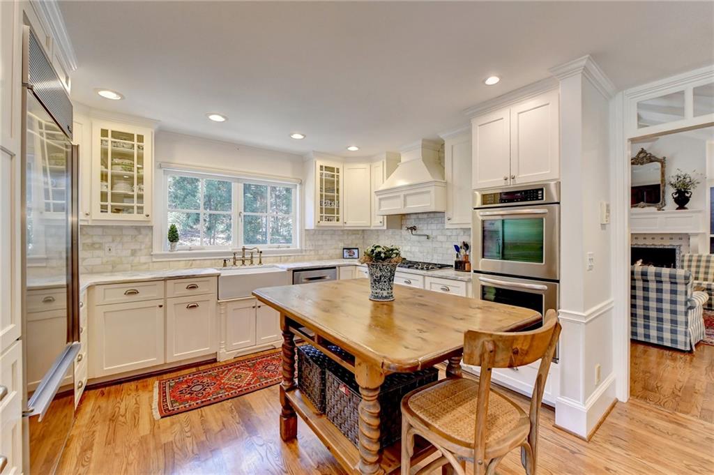 Kitchen featuring white cabinetry, custom range hood, appliances with stainless steel finishes, light hardwood / wood-style floors, and sink