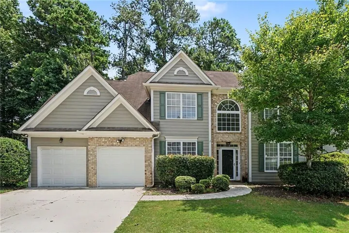 Two-story home with a two-car garage, brick accents, arched window, and mature landscaping