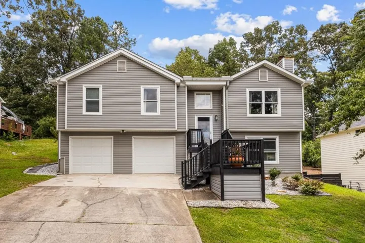 Split-level residence featuring gray siding, a two-car garage, and a front deck with dark railings