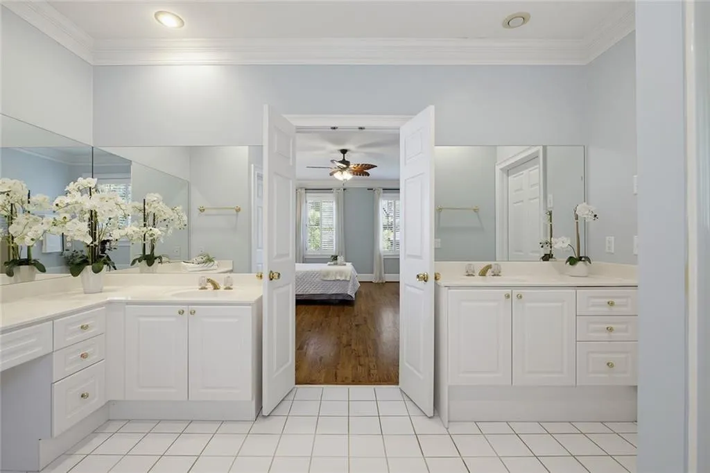 Dual vanities with white cabinetry, integrated sinks, large mirrors, and gold-tone hardware