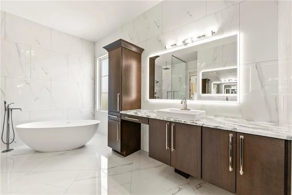 Primary bathroom with tile walls, vanity, free-standing solid-surface 6-ft tub, light marble finish floors, and a walk in shower Primary bath featuring light marble finish floors, vanity, a marble finish shower, plenty of natural light, and tile walls, a spa bath.