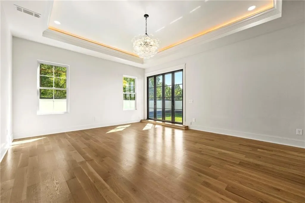 Primary suite on the third level featuring a raised ceiling, a chandelier, wood finished floors, and ornamental molding