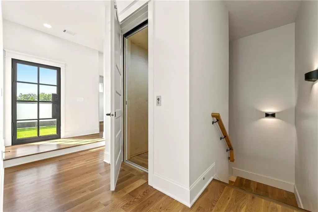 Third level Primary suite with stairs featuring wood finished floors, view of the elevator and doors that lead to the spacious outdoor terrace Third level Primary suite with stairs featuring wood finished floors, view of the elevator and doors that lead to the spacious outdoor terrace