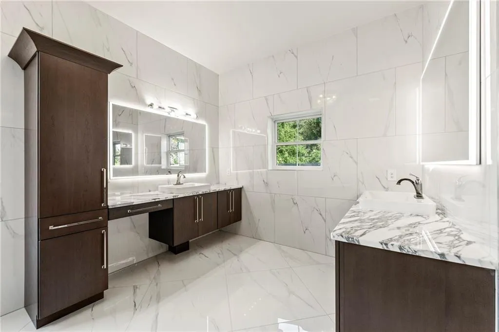 Primary bathroom featuring tile walls, two vanities, and light marble finish floors Primary bathroom featuring tile walls, two vanities, and light marble finish floors