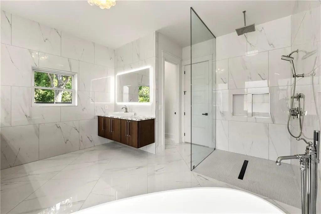Primary bath featuring light marble finish floors, vanity, a marble finish shower, plenty of natural light, and tile walls, a spa bath featuring a luxury, free-standing solid-surface 6-ft tub—opens to a large private terrace Primary bath featuring light marble finish floors, vanity, a marble finish shower, plenty of natural light, and tile walls, a spa bath featuring a luxury, free-standing solid-surface 6-ft tub—opens to a large private terrace