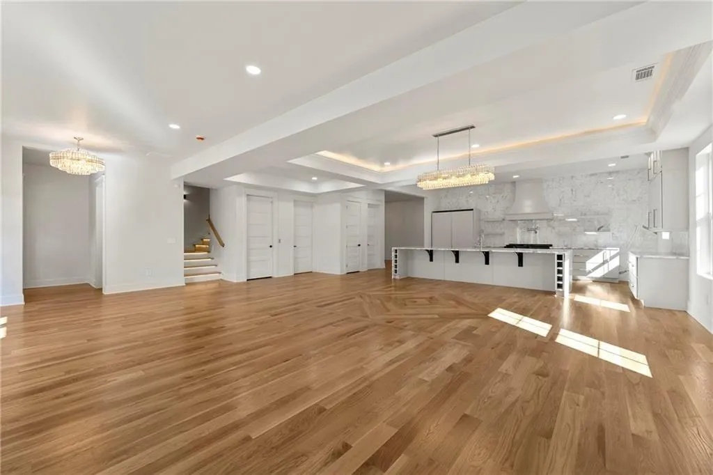 Living room with a chandelier, a raised ceiling, stairs, light wood-floors, and recessed lighting Living room with a chandelier, a raised ceiling, stairs, light wood-floors, and recessed lighting