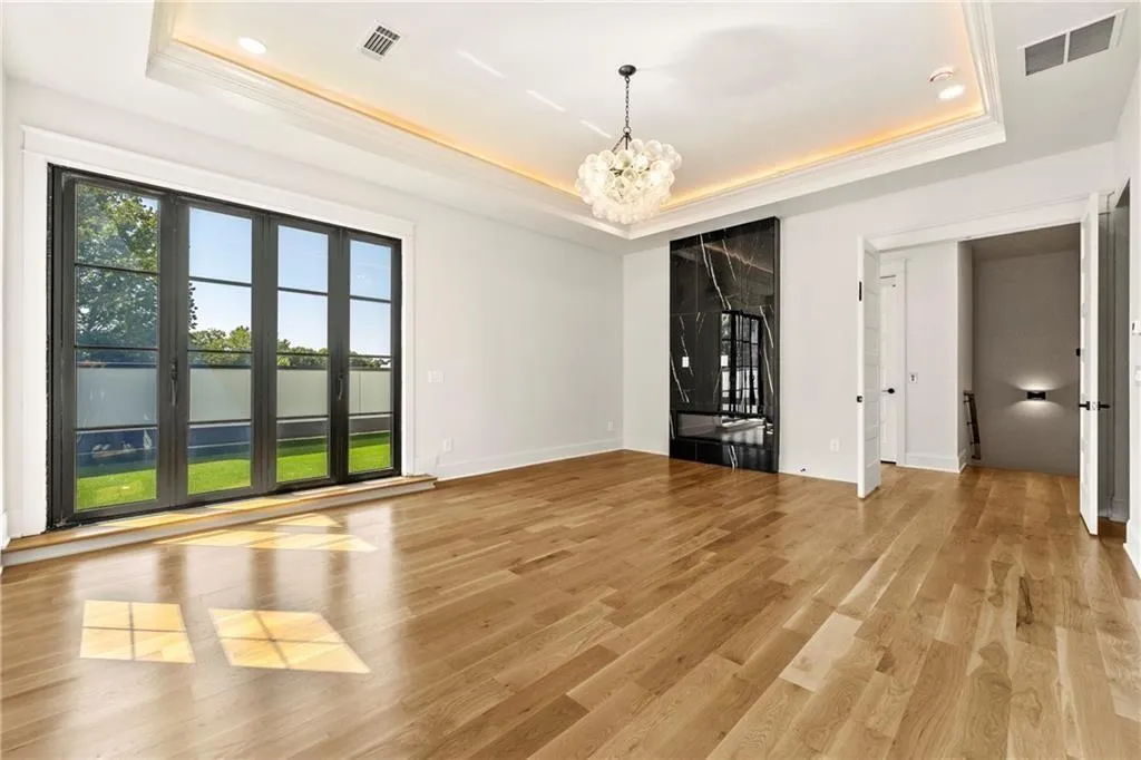 Primary suite on the third level with a tray ceiling, light wood-floors, and a chandelier.