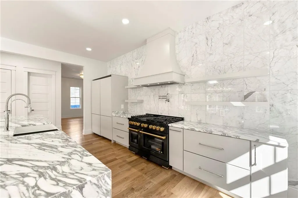 Kitchen featuring marble countertops, custom range hood, range with two ovens, light wood-flooring, and recessed lighting Kitchen featuring marble countertops, custom range hood, range with two ovens, light wood-flooring, and recessed lighting