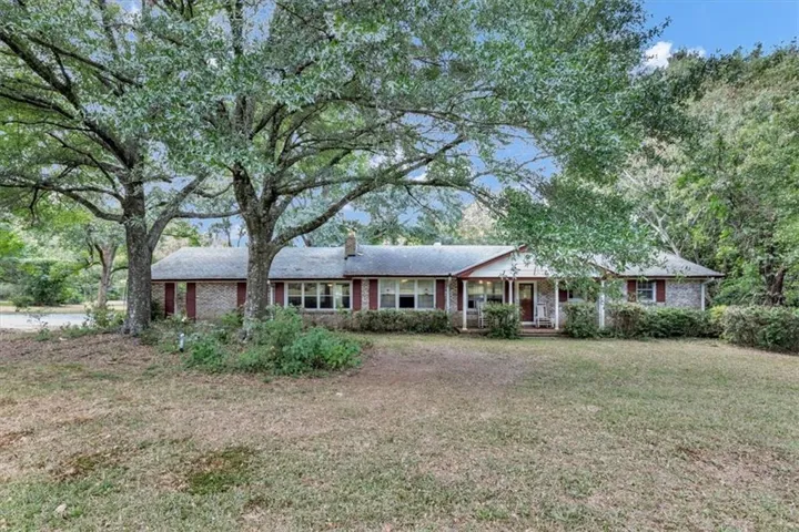 Brick exterior with a gabled roofline, mature trees, a covered porch with white columns, and red window shutters