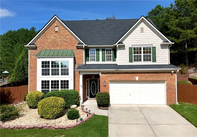 Two-story residence featuring a brick facade with complementary siding, a two-car garage, and a bay window with a green metal roof accent