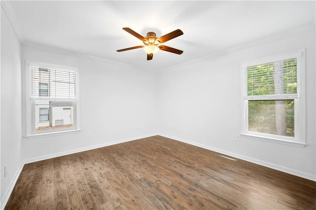 Spare room with crown molding, healthy amount of natural light, dark wood-type flooring, and a ceiling fan