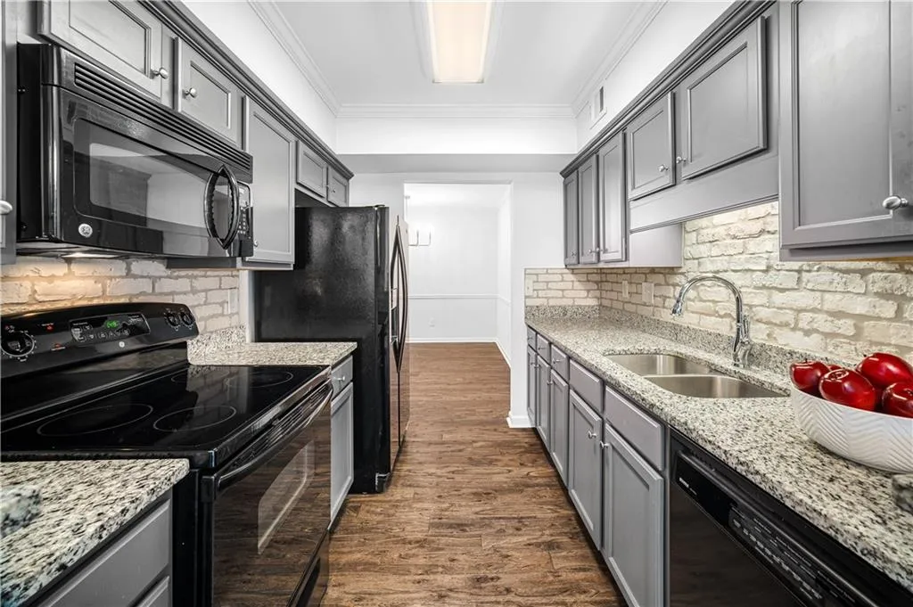 Kitchen with black appliances, gray cabinetry, light stone countertops, ornamental molding, and tasteful backsplash