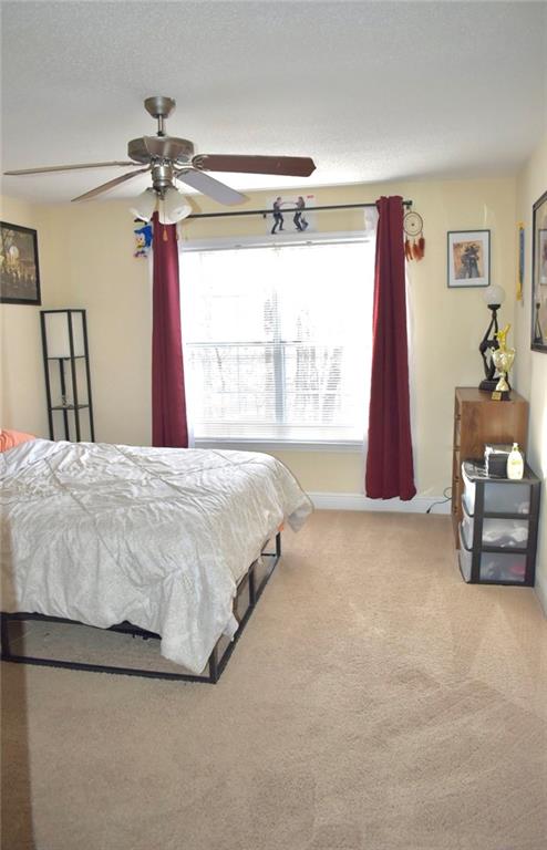 Carpeted bedroom with large window, a textured ceiling, and ceiling fan
