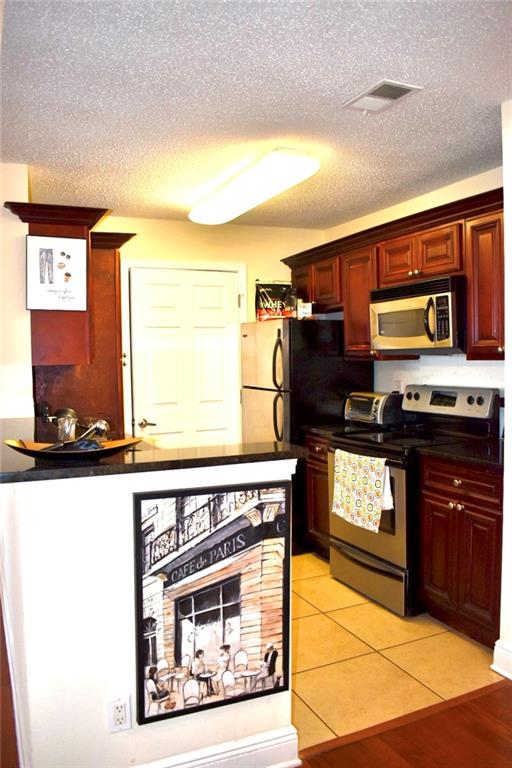 Kitchen featuring appliances with stainless steel finishes, a textured ceiling, and light style flooring