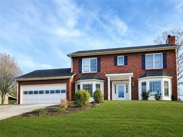Brick exterior with a covered entry, two bay windows, a two-car garage, and a sloped lawn