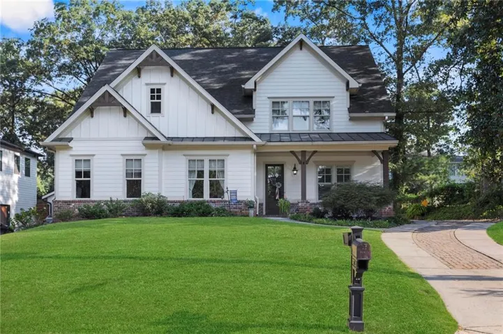 White siding exterior with dark trim accents, gabled roofline, stone foundation, covered front porch with wood columns, and a paved driveway