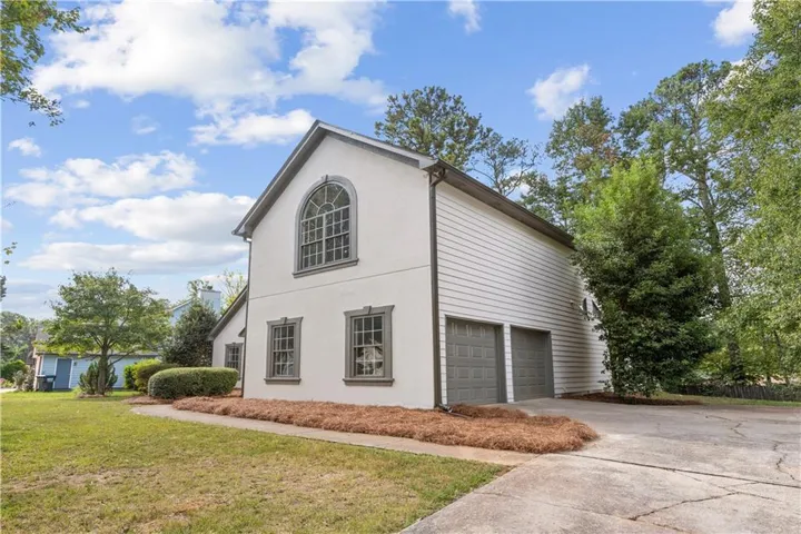 Stucco and siding exterior, arched window, attached two-car garage, concrete driveway, and mature landscaping