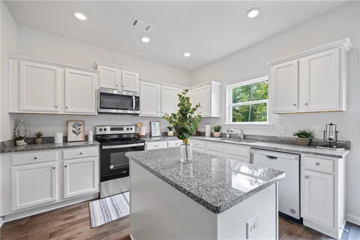 Kitchen featuring white cabinetry, granite countertops, stainless steel appliances, a center island, and wood-finish flooring