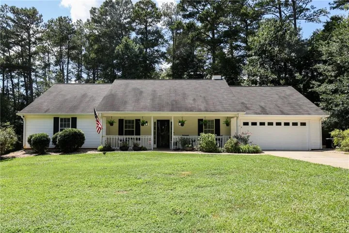 White siding exterior with a covered front porch, dark shutters, an attached garage, and mature landscaping