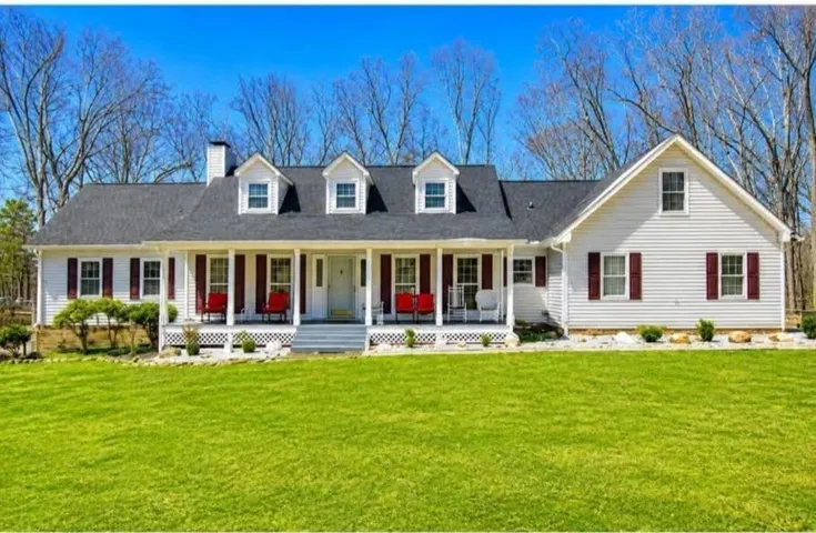 Classic Colonial-style residence featuring a wraparound front porch with white columns, dormer windows with shutters, and a charcoal-gray pitched roof