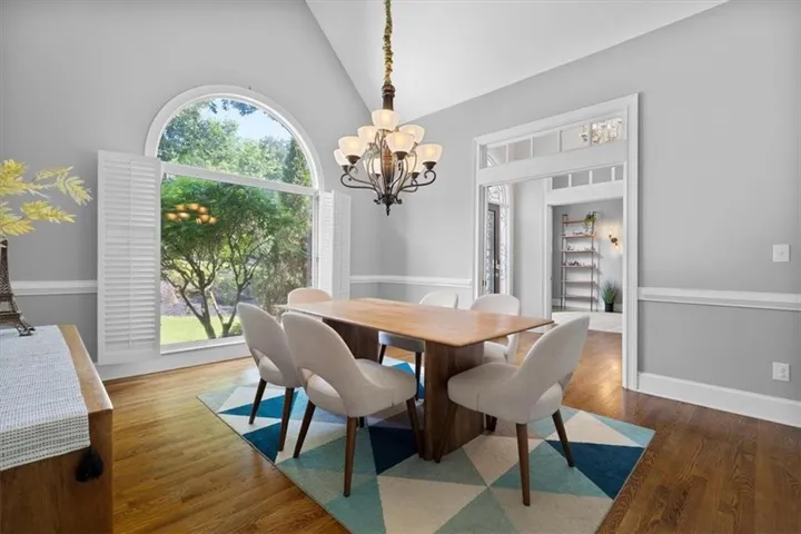 Dining area featuring a prominent arched window with white plantation shutters, a multi-tier chandelier, wood-finish flooring, and crown molding