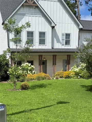 Two-story residence featuring white board and batten siding, a gray shingle roof, and a gabled dormer with exposed timber framing