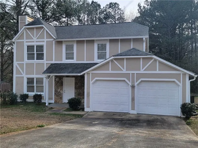 Tudor-style house featuring roof with shingles, concrete driveway, a chimney, and stucco siding