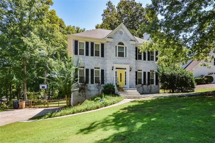 Two-story brick exterior with a prominent gabled entry, black window shutters, and a bright yellow front door