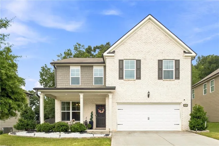 Two-story exterior featuring a brick facade, covered porch with columns, attached two-car garage, and established landscaping