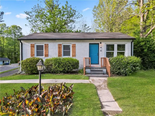 White brick exterior with a teal front door, wood-tone shutters, and a wood-tone railing