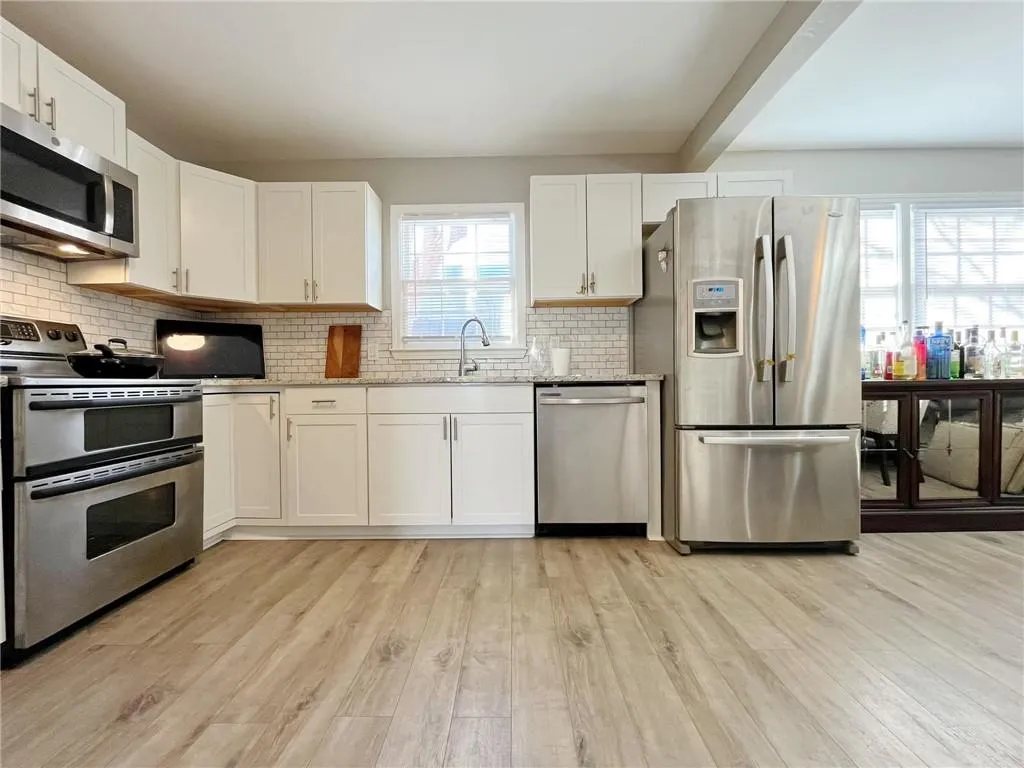 Kitchen featuring stainless steel appliances, white cabinets, light wood-style flooring, backsplash, and beam ceiling