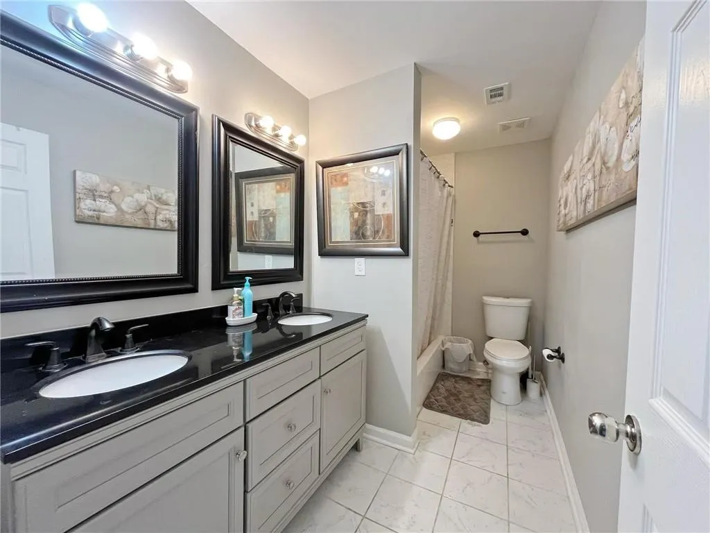 Full bath featuring light marble finish floors, double vanity, and shower / bath combo with shower curtain