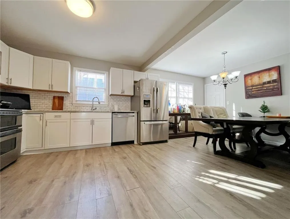 Kitchen featuring suspended lighting, stainless steel appliances, white cabinets, light wood-style flooring, and light stone counters