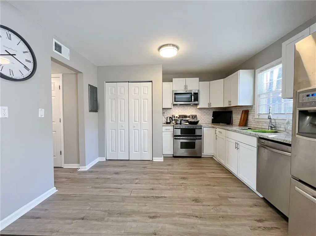 Kitchen with stainless steel appliances, white cabinets, decorative backsplash, and light wood-style floors