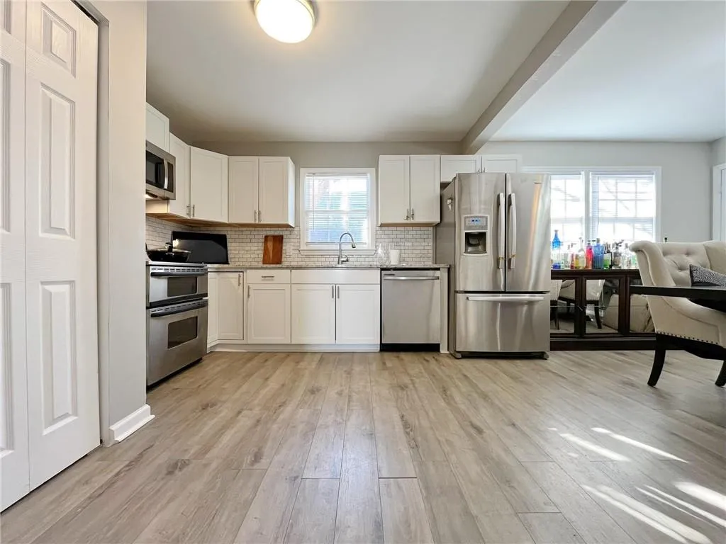 Kitchen featuring stainless steel appliances, white cabinetry, light wood-style floors, decorative backsplash, and beamed ceiling
