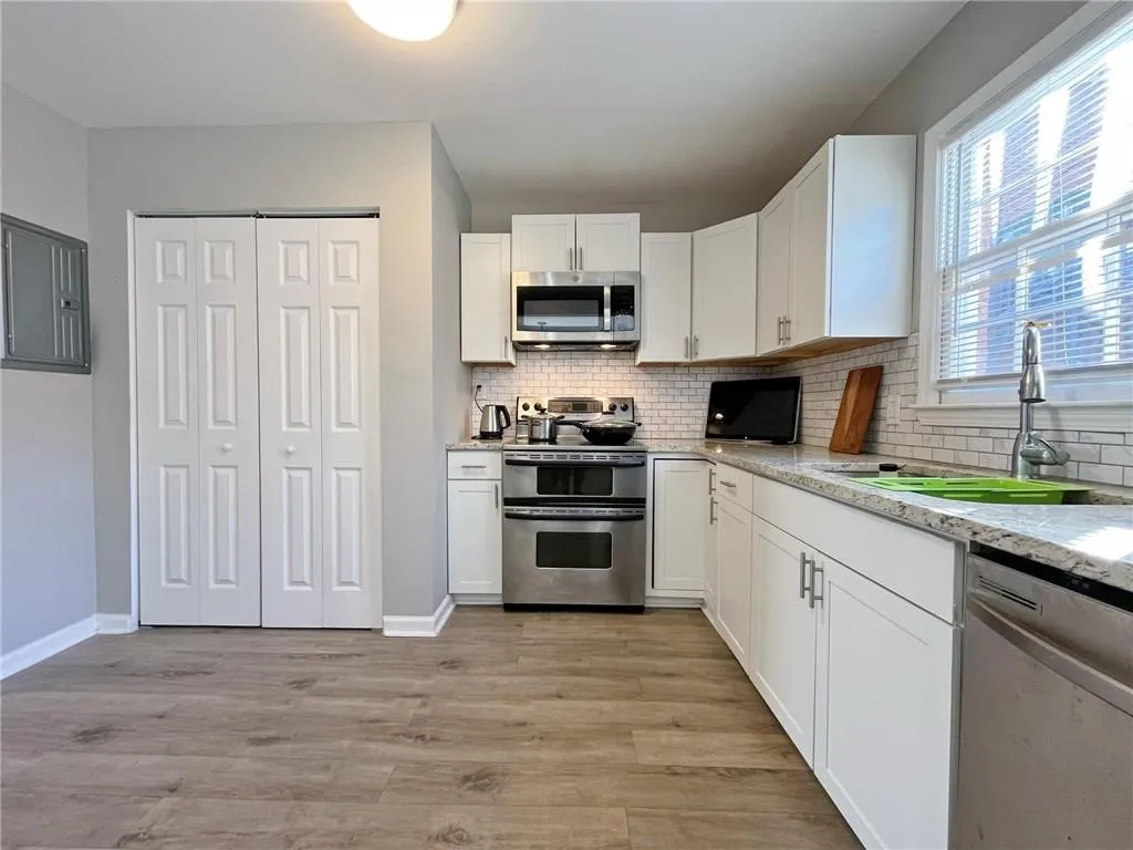 Kitchen with stainless steel appliances, white cabinetry, electric panel, light wood finished floors, and light stone countertops